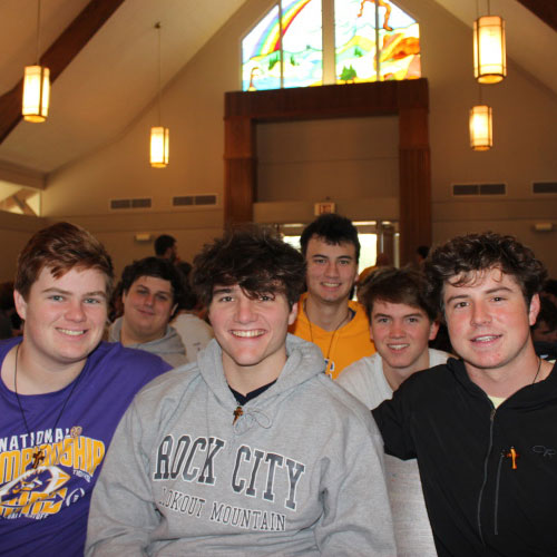 A group of six young men from St. Paul's School sit indoors, smiling at the camera, with stained glass and ceiling lights in the background.