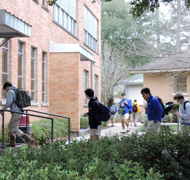 Students with backpacks walk toward St. Paul's School, a school for boys northshore LA, entering the brick building on a cloudy day.