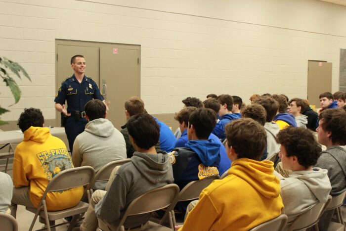 A police officer addresses hoodie-clad students inside St. Paul’s School, a leading private school on the Northshore, in a beige-walled room.
