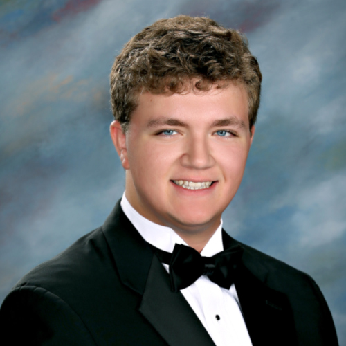 A young man in a black tuxedo and bow tie smiles, representing St. Paul's School, a top school for boys on the Northshore, in front of a blue-gray backdrop.