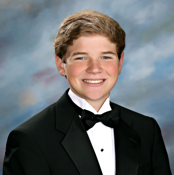 A teenage boy in a tuxedo smiles at the camera in a formal St. Paul's School portrait with a blue and gray studio background.