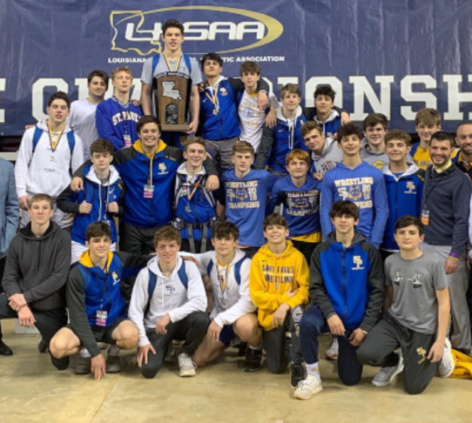 A group of St. Paul's School wrestlers and coaches pose together in front of an LHSAA championship banner.