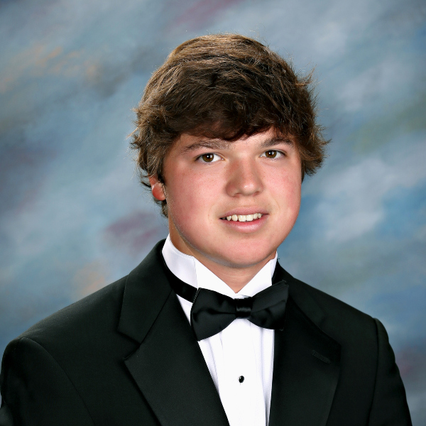 A young man in a black tuxedo and bow tie poses for a formal portrait, representing St. Paul’s School against a blue and gray studio background.