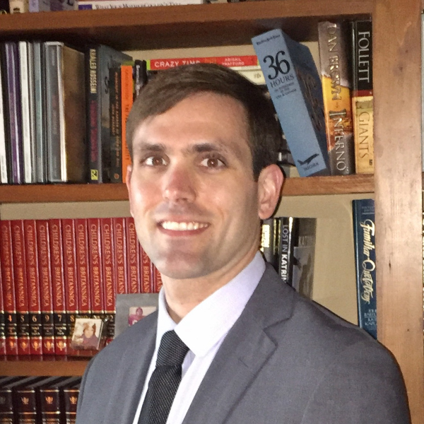 A man in a suit and tie stands before a bookshelf, reflecting the tradition of private schools on the Northshore like St. Paul's School.