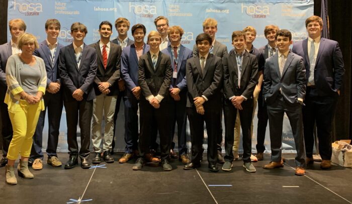 A group from St. Paul's School, a top school for boys northshore LA, poses in suits at a HOSA Louisiana event backdrop with one woman in business attire.