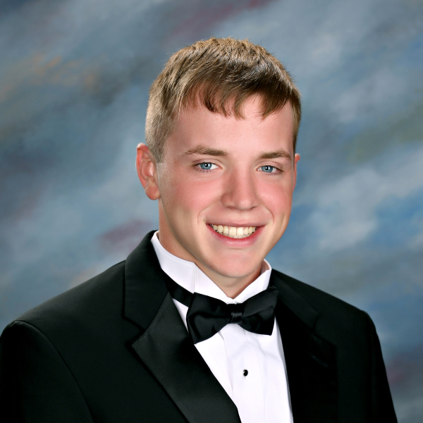 A young man in a black tuxedo represents St. Paul’s School, smiling confidently before a blue and gray mottled background.