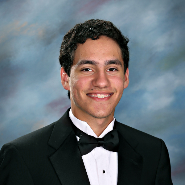 Young man in a black tuxedo and bow tie, smiling in front of a blue and gray studio backdrop at St. Paul's School.