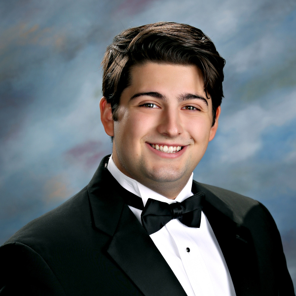 Young man in a black tuxedo, smiling before a blue-gray backdrop at St. Paul's School, a leading school for boys on the Northshore, LA.