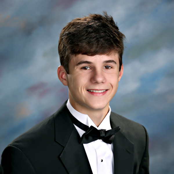 A young man in a tuxedo and bow tie poses and smiles for a formal portrait, representing St. Paul's School for boys on the Northshore.