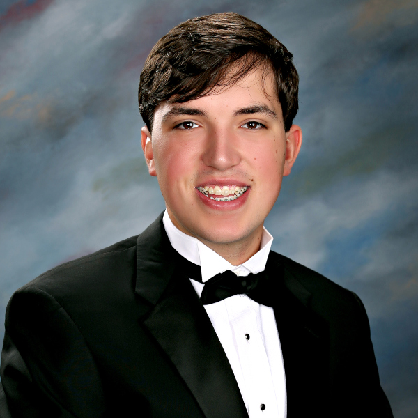 Young man with short brown hair in a black tuxedo, posing before a blue-gray backdrop at St. Paul’s School, a top boys’ school on the Northshore.