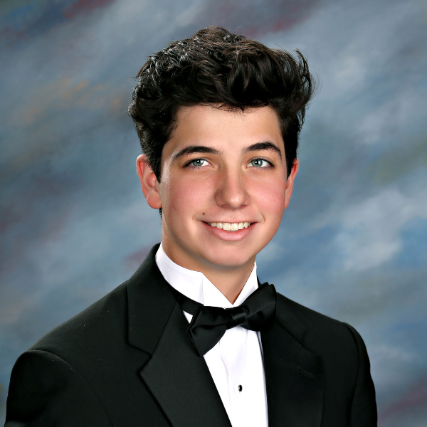 A young person in a tuxedo smiles in front of a blue and gray studio backdrop at St. Paul's School, a leading school for boys on the Northshore.