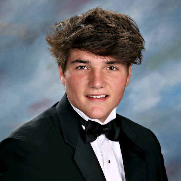 A young person in a black tuxedo and bow tie poses before a softly blurred backdrop, representing St. Paul's School for boys Northshore LA.