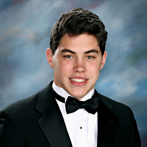 A young man in a black tuxedo and bow tie poses for a formal St. Paul's School portrait against a blue-gray studio background.
