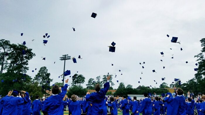 Graduates in blue gowns from St. Paul's School toss their caps into the air outdoors, with trees and lights in the background.