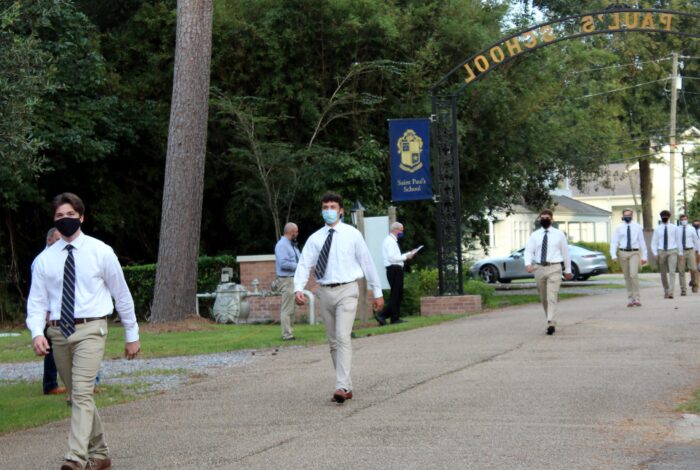 Several students in uniform and masks walk on the St. Paul's School campus, a leading school for boys northshore LA, under a 