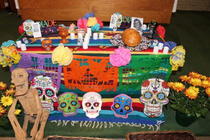 A Día de los Muertos altar at St. Paul’s School with vibrant decorations, sugar skulls, candles, flowers, bread, and a wooden skeleton.