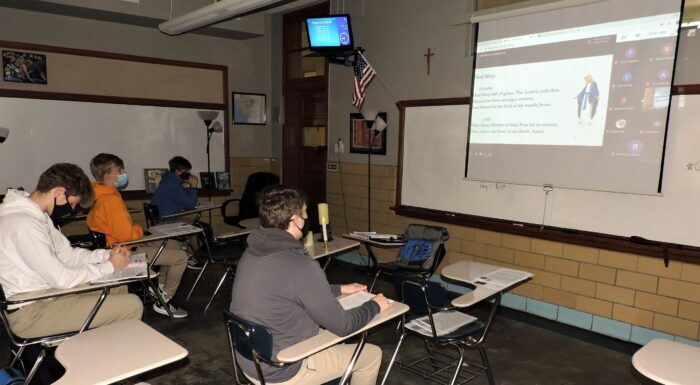 Students in masks sit at desks at St. Paul's School, watching a whiteboard presentation at this school for boys Northshore LA.