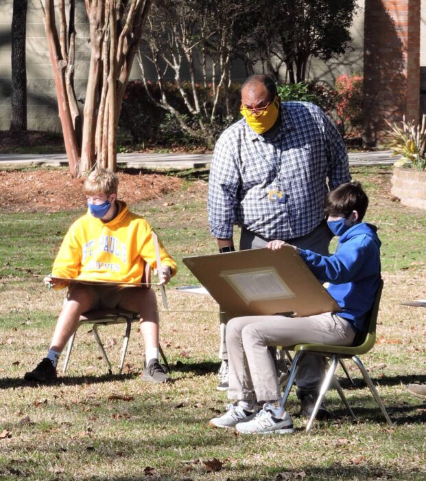 Two students wearing masks draw outdoors at St. Paul's School as a masked adult observes—an example of private schools on the northshore.