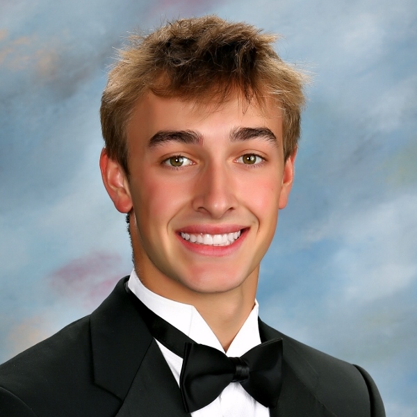 Young man in a black tuxedo and bow tie, smiling proudly—representing St. Paul's School against a soft blue-gray studio background.