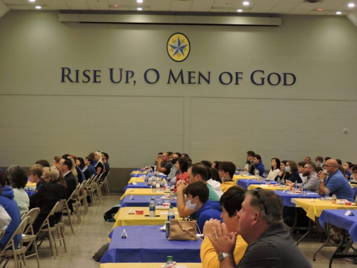 A group gathers in a hall at St. Paul's School, with a sign on the wall reading 