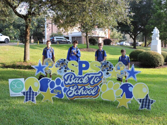 Four boys in St. Paul's School uniforms stand outside by a 