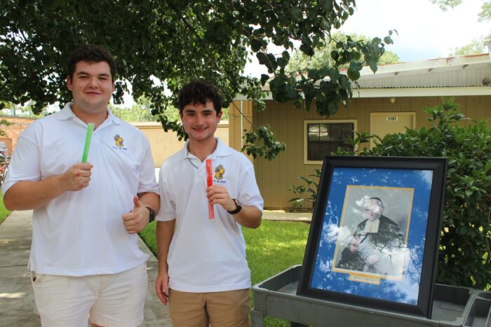 Two young men in white shirts enjoy ice pops outdoors at St. Paul's School, standing by a framed photo with trees and a building behind them.