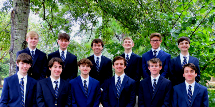 Thirteen young men in navy suits and striped ties from St. Paul’s School pose outdoors, a distinguished school for boys northshore LA.