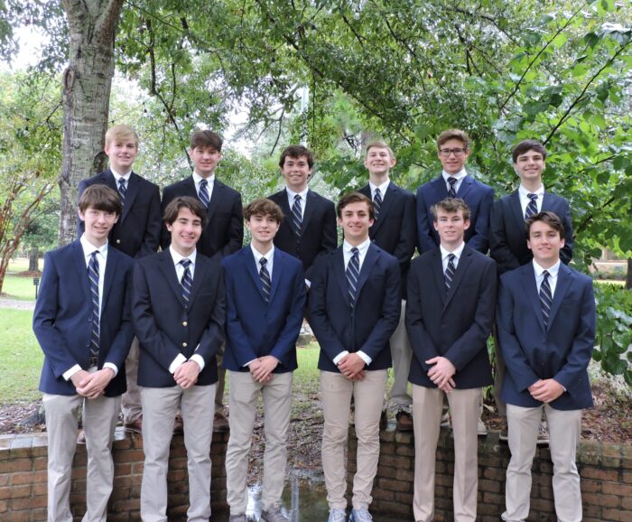 Thirteen boys in khakis and blazers pose outdoors at St. Paul's School, a leading school for boys Northshore LA, before green trees and brick wall.