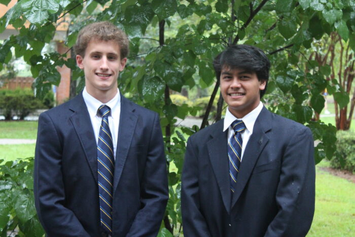 Two young men in suits and striped ties stand outdoors at St. Paul’s School, both smiling at the camera.