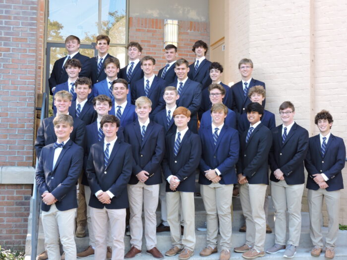 Twenty-four young men from St. Paul's School in blue blazers and ties pose on stairs outside a brick building for a group photo.