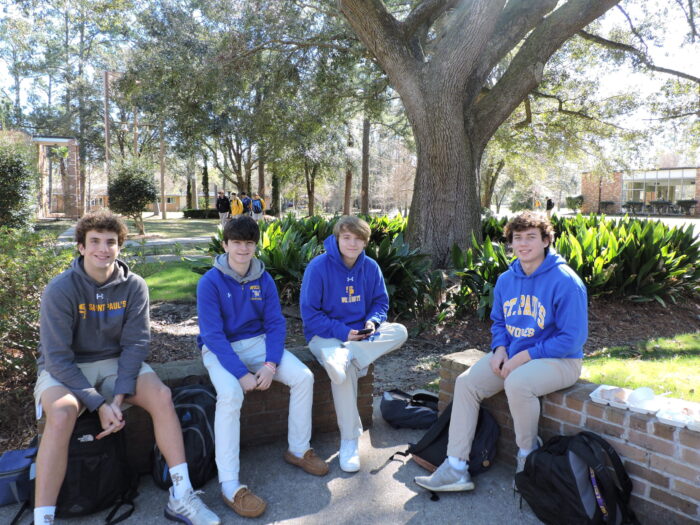 Four teenage boys sit on a brick ledge outdoors, wearing St. Paul’s School hoodies—one of the top private schools on the Northshore.