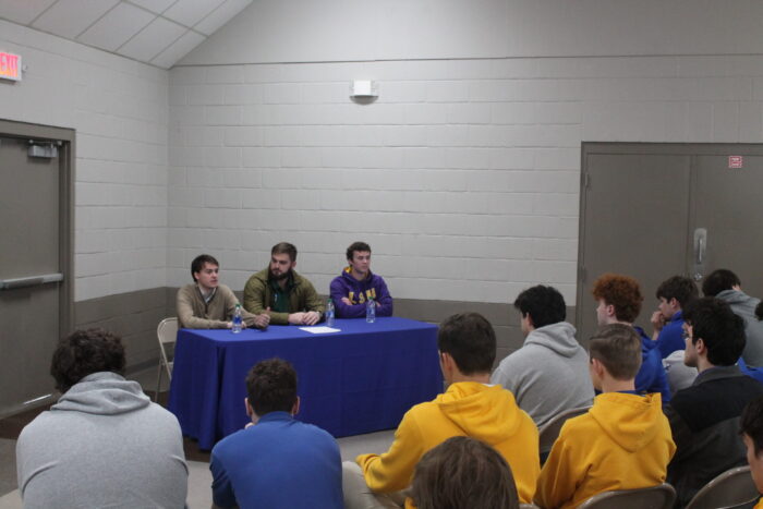 Three men address young people at St. Paul’s School, a renowned school for boys on the Northshore, sitting behind a blue tablecloth.