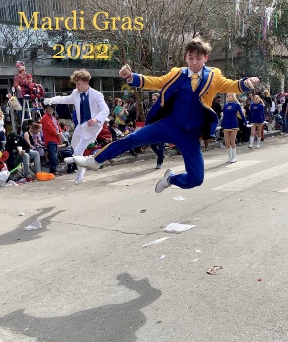 Two young men from St. Paul's School jump mid-air at a Mardi Gras parade, with onlookers and cheerleaders behind. Text reads 