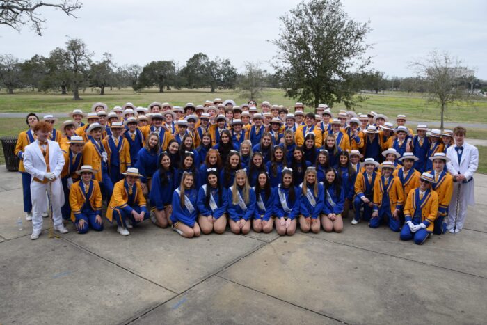 A large group in blue and yellow uniforms from St. Paul's School poses outdoors for a group photo on a cloudy day.