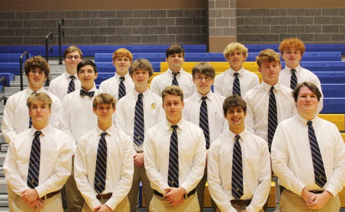 Sixteen young men in white shirts and striped ties pose in bleachers at St. Paul’s School, a leading school for boys on the Northshore.