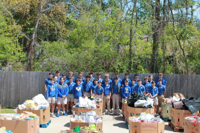 A group from St. Paul's School stands outdoors behind boxes of donated items, with trees and a fence behind this school for boys northshore LA.