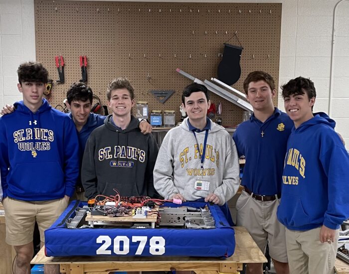 Six students in St. Paul's School Wolves shirts stand behind a blue robot labeled 2078 in a workshop with tools on the wall.