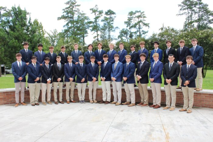 A group of young men from St. Paul's School in blazers and ties pose outdoors by trees and a brick wall.