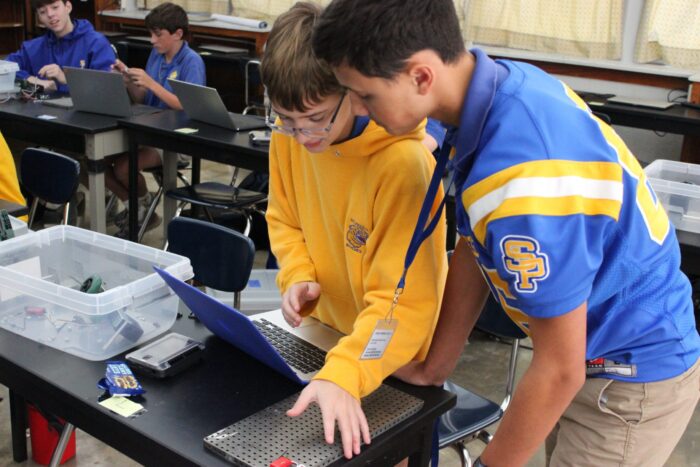 Two students at St. Paul's School collaborate on robotics projects in a lively classroom with peers in the background.