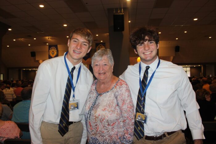 Three people pose indoors; two young men from St. Paul’s School stand on either side of an older woman in a floral top.