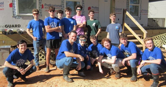 A group from St. Paul's School, mostly in blue shirts, poses for a photo outside a house under construction on a sunny day.