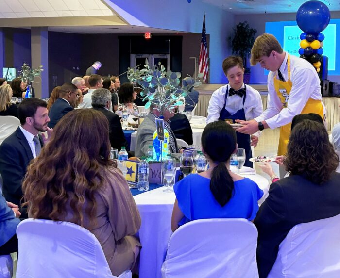 Two young men from St. Paul's School serve food at a formal event with blue and yellow decor on the Northshore.