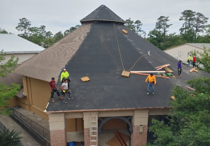 Several workers install materials on a steep, black-roofed building at St. Paul's School, surrounded by trees and construction supplies.