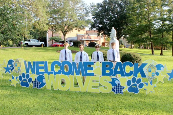 Four boys in white shirts and ties at St. Paul's School stand by a “Welcome Back Wolves” sign on the lawn of this school for boys Northshore, LA.