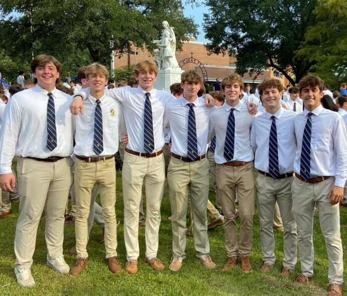 Seven young men in uniform smile outside on the grass at St. Paul's School, a leading school for boys on the Northshore, with a statue behind them.