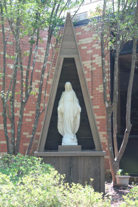 A white statue of a woman stands in a wooden alcove at St. Paul's School, a leading private school on the Northshore, amid trees and plants.