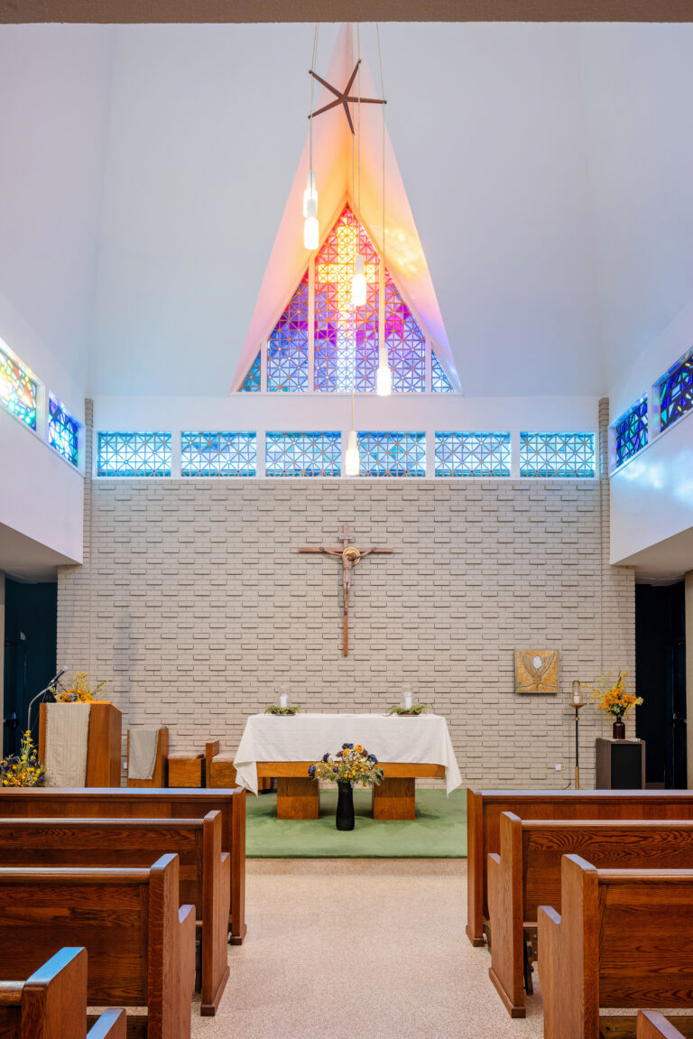 A church altar with a crucifix, stained glass, and wooden pews, as seen at St. Paul’s School for boys on the Northshore.