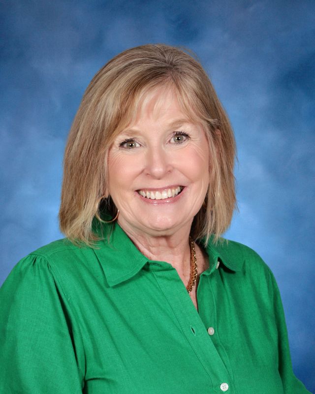 A woman with shoulder-length blonde hair in a green shirt smiles, representing St. Paul's School against a blue background.