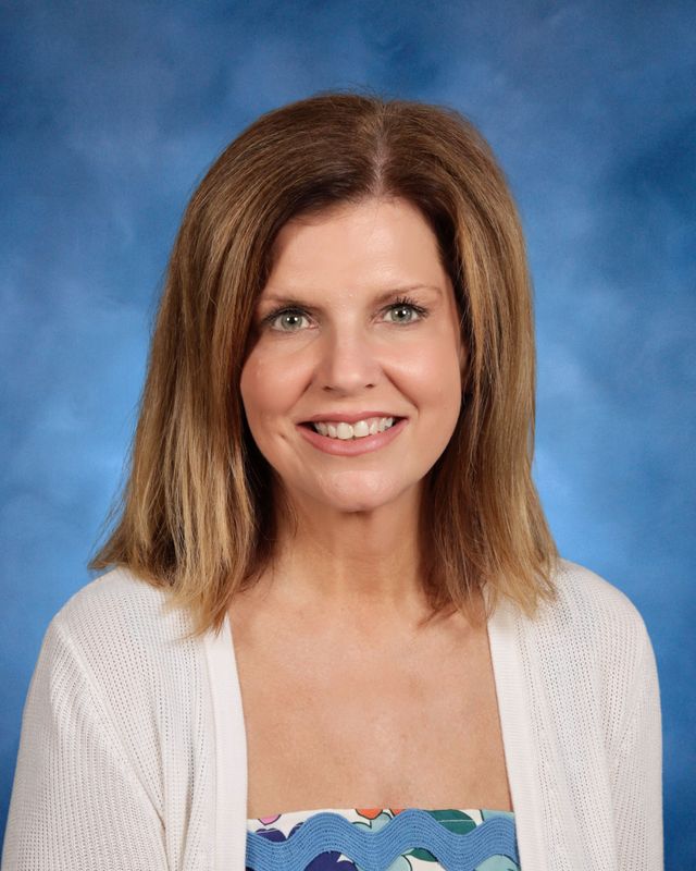 A woman with shoulder-length light brown hair smiles in front of a blue background, representing St. Paul’s School on the Northshore.