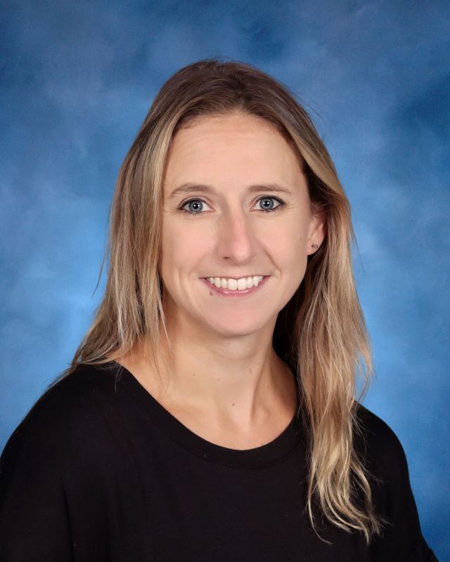 A woman with long blonde hair wearing a black top, smiling at the camera against a blue studio background at St. Paul’s School.